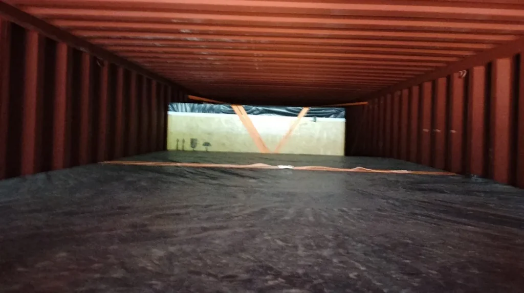 Zabezpieczenie ładunku w kontenerze – skrzynia drewniana unieruchomiona pasami mocującymi podczas transportu eksportowego.